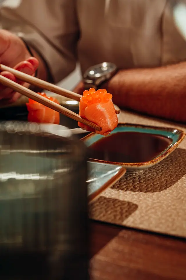 Pauzinhos a mergulhar um nigiri de salmão no molho de soja