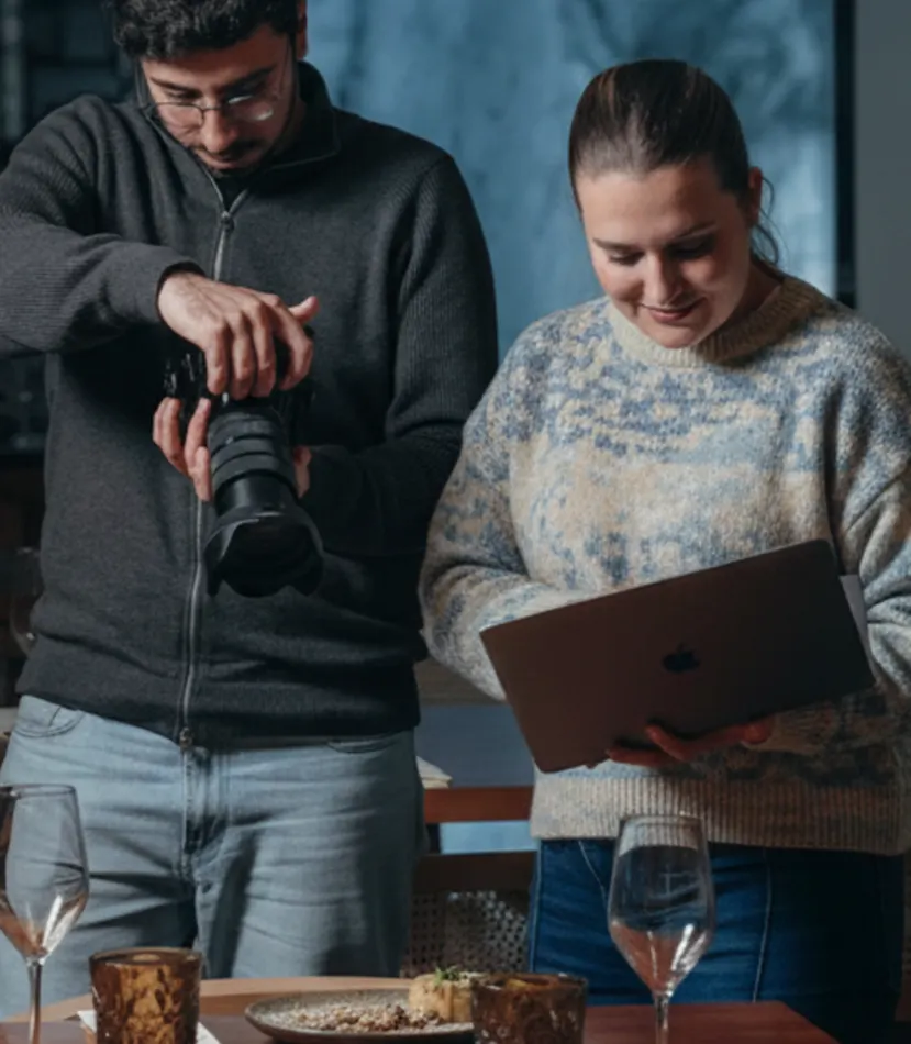 A Sofia e o Pedro à mesa de um restaurante, ele com a câmara e ela com o portátil
